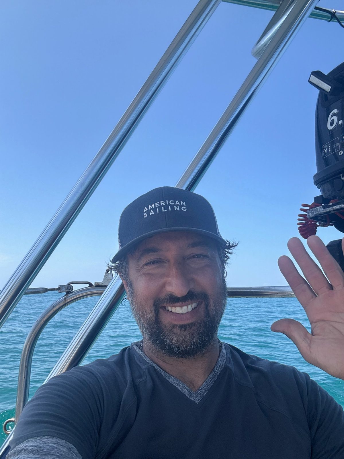 Captain Jason Pisaro waving from the cockpit of Yemaya with turquoise water behind him