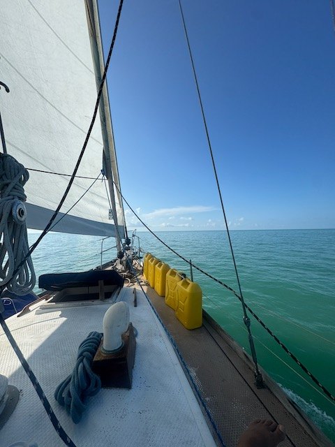 Foredeck and side deck of Yemaya with jerry cans lashed along the rail, green water beyond